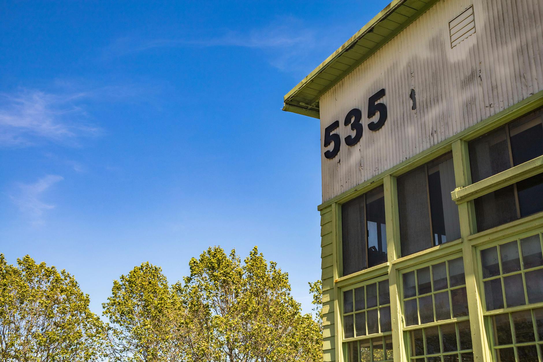 Corner of an industrial building with number 535, trees, and a clear blue sky.