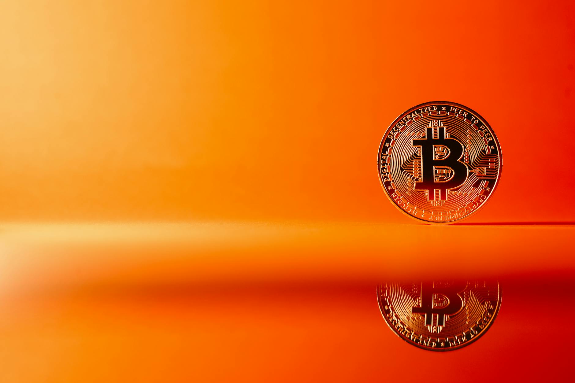 Golden Bitcoin with reflection on a bright orange background, representing digital currency concepts.