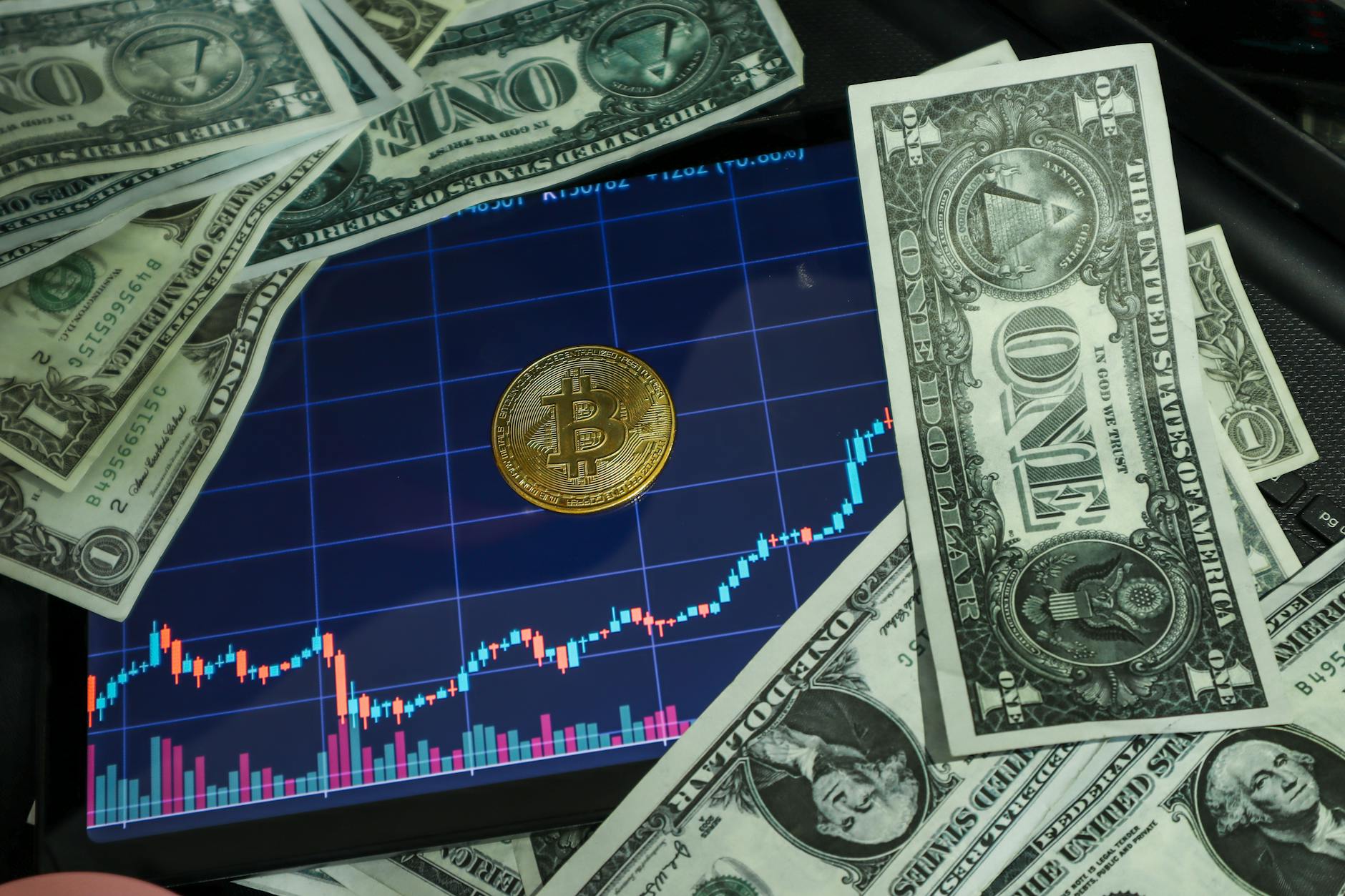 Bitcoin coin on a tablet showing stock chart, surrounded by dollar bills.