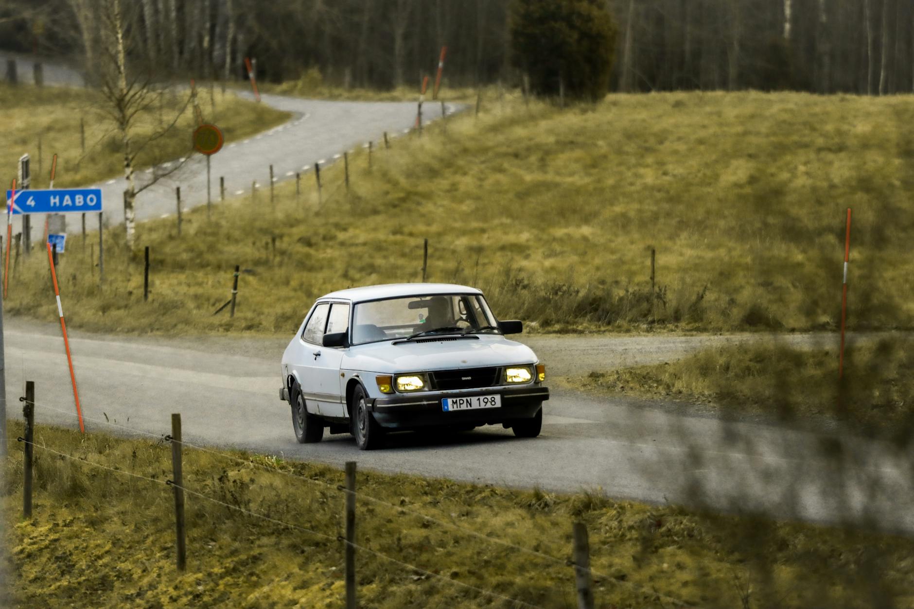 Vintage car navigates a scenic rural road in Habo, Sweden, under a cloudy winter sky.