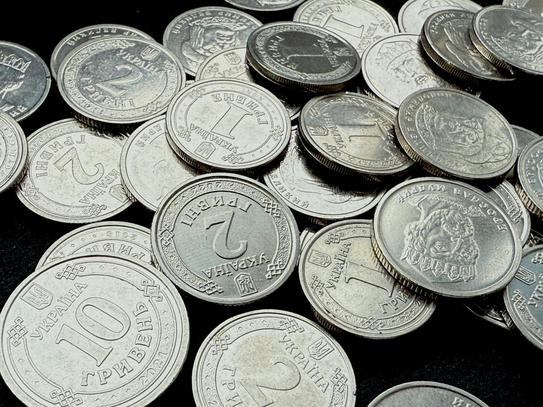 Close-up of Ukrainian Hryvnia coins scattered against a dark background, showing detailed engravings.