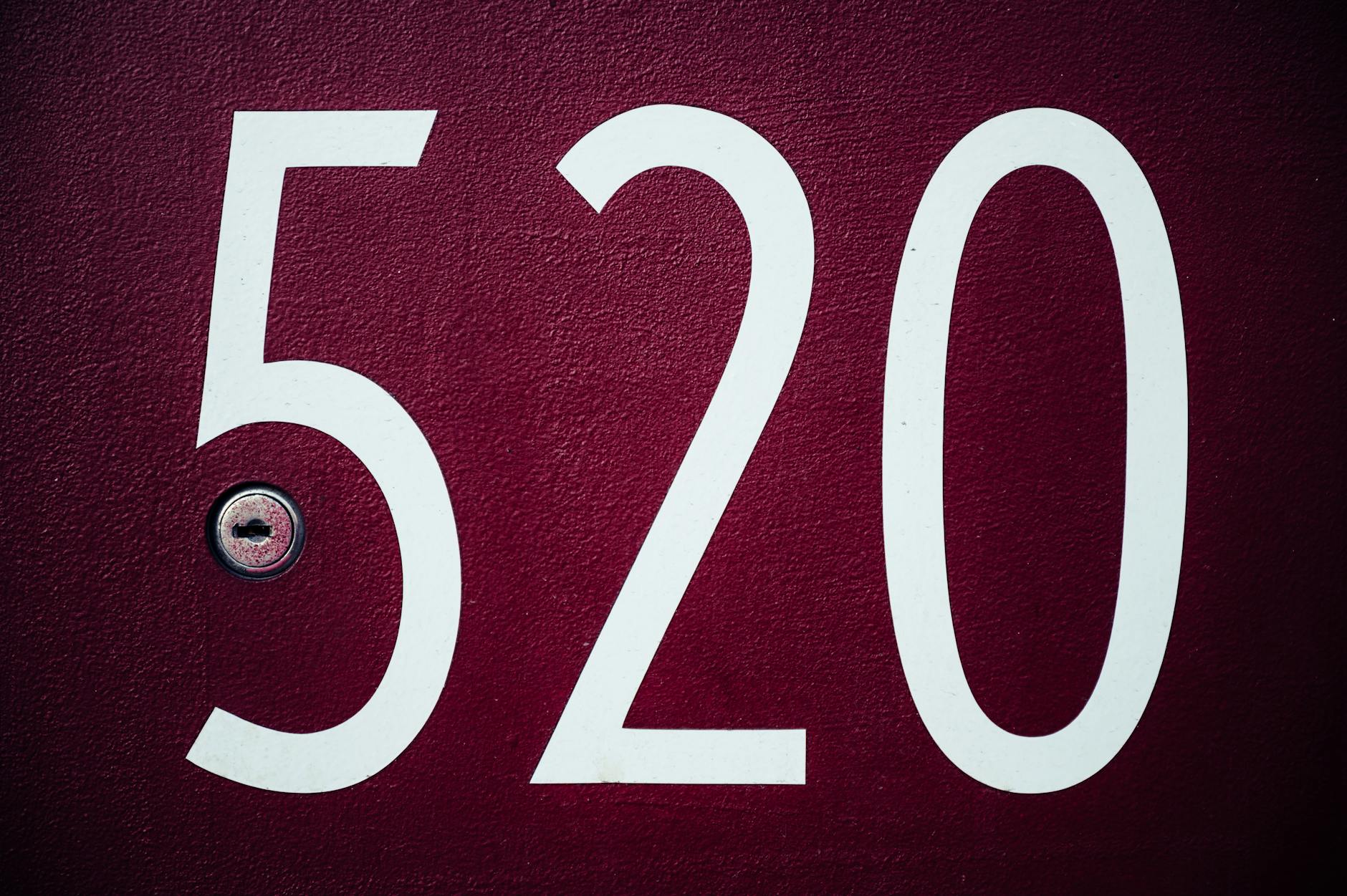Number 520 in big white digits on rough textured red surface of door with small metal keyhole