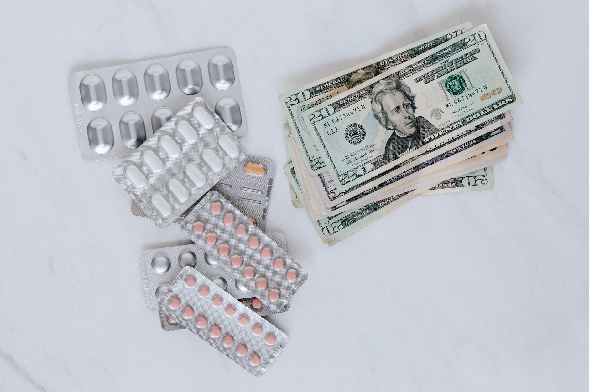 From above of silver blister full of drug near big pile of dollar to spend on medication