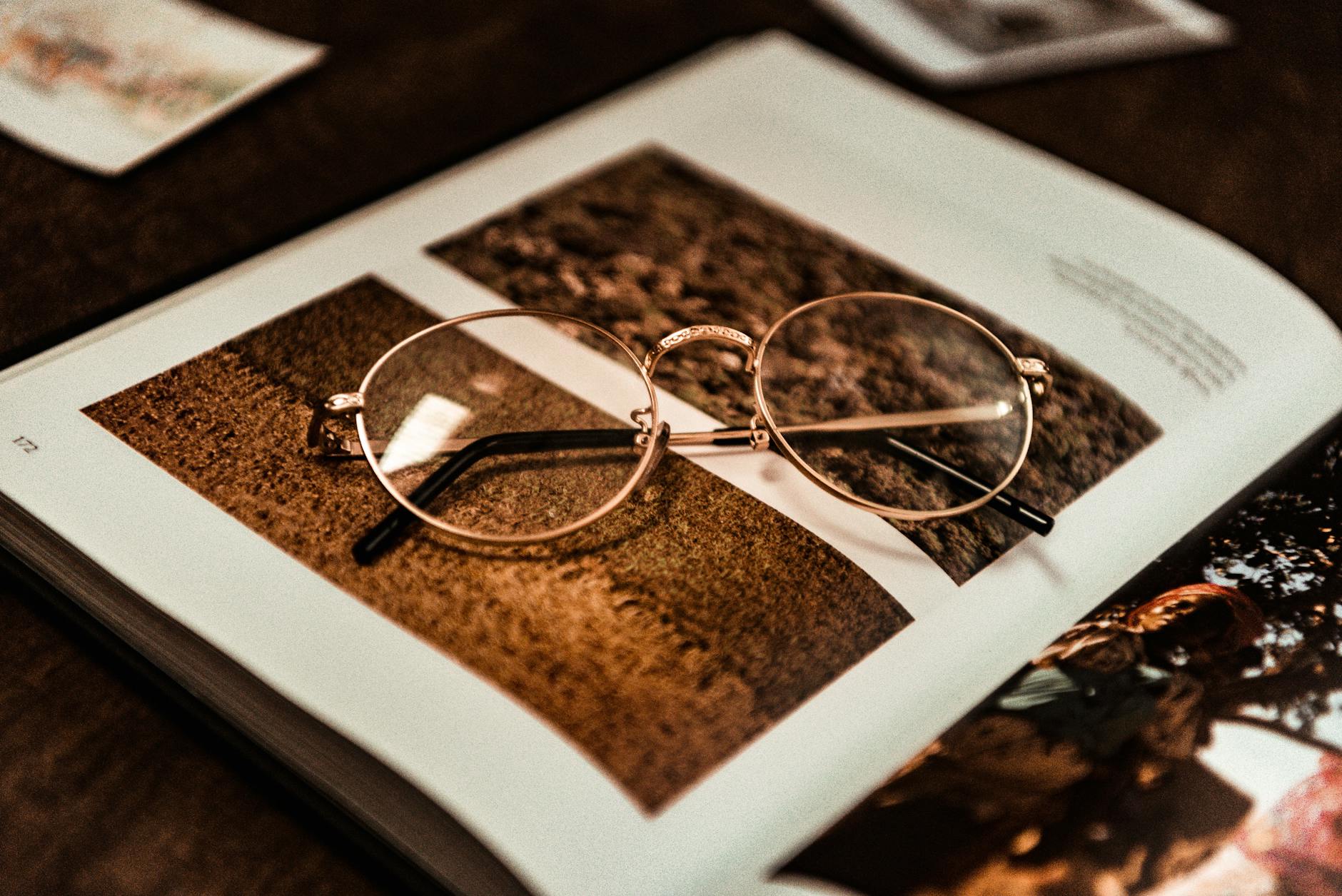 Close-up of vintage eyeglasses resting on an open magazine with photos.