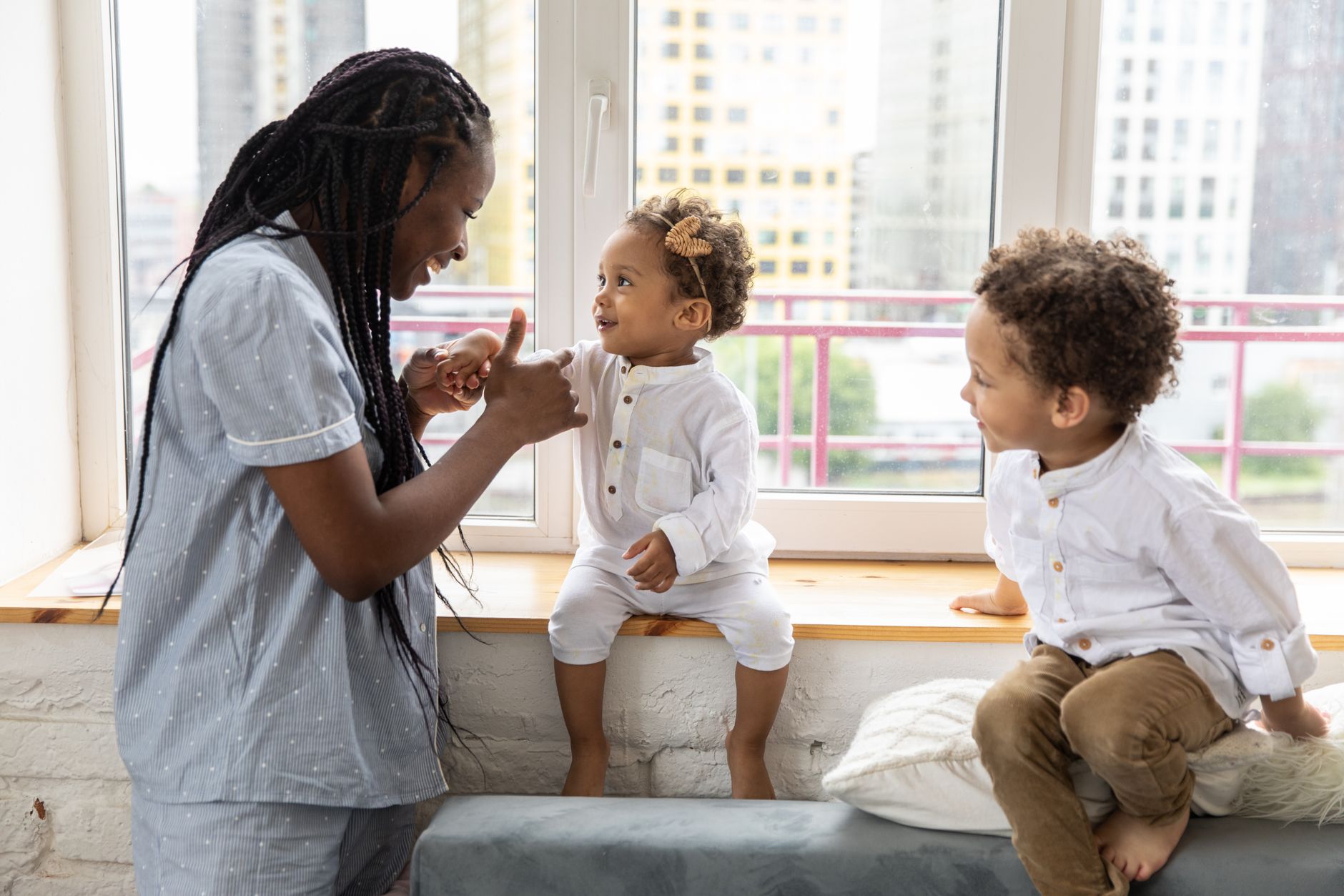 A mother and her young children enjoying playful interaction on a windowsill indoors.