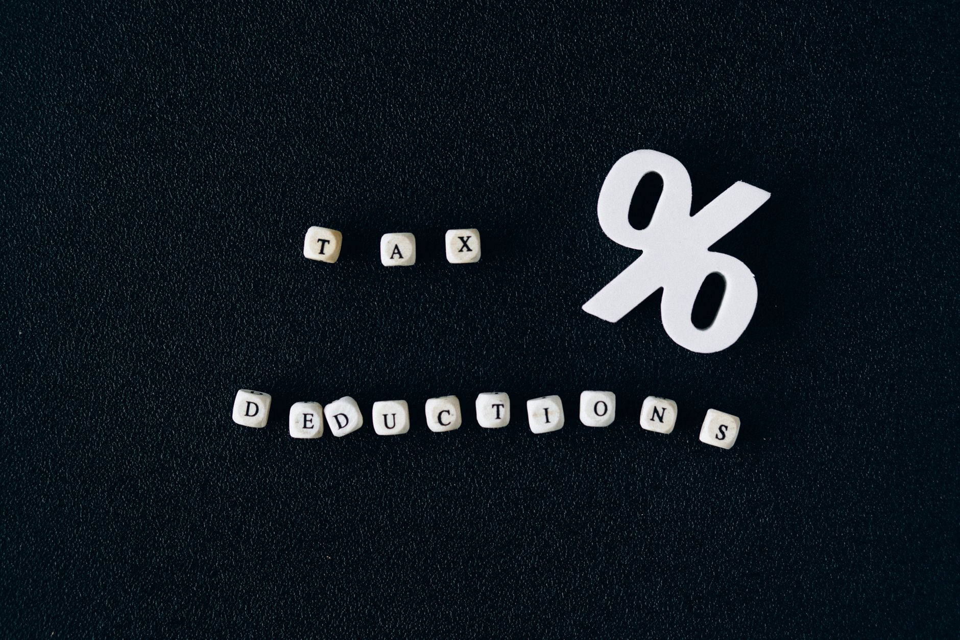 Conceptual image of tax deductions with alphabet blocks and percent symbol on black surface.