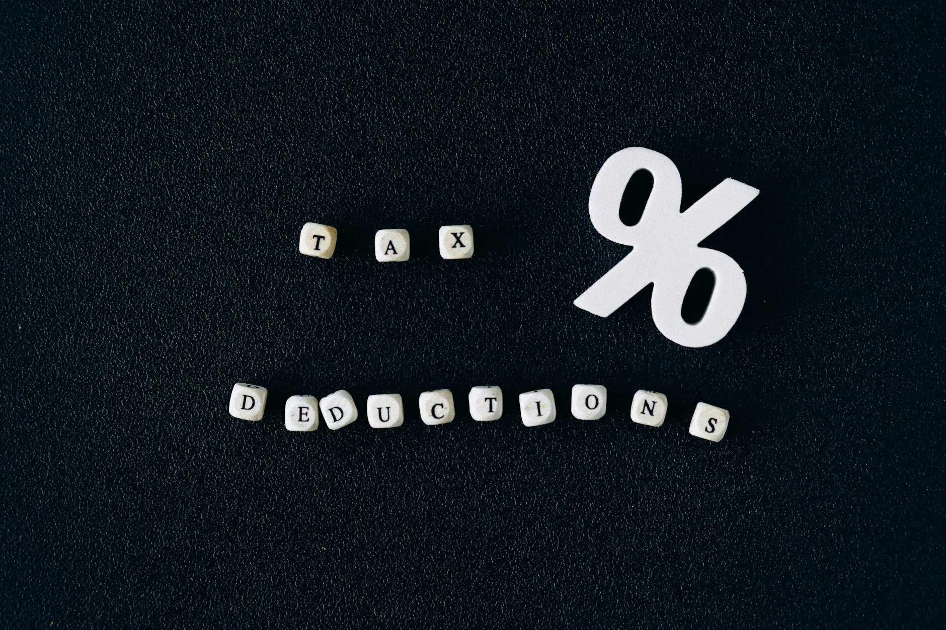 Conceptual image of tax deductions with alphabet blocks and percent symbol on black surface.