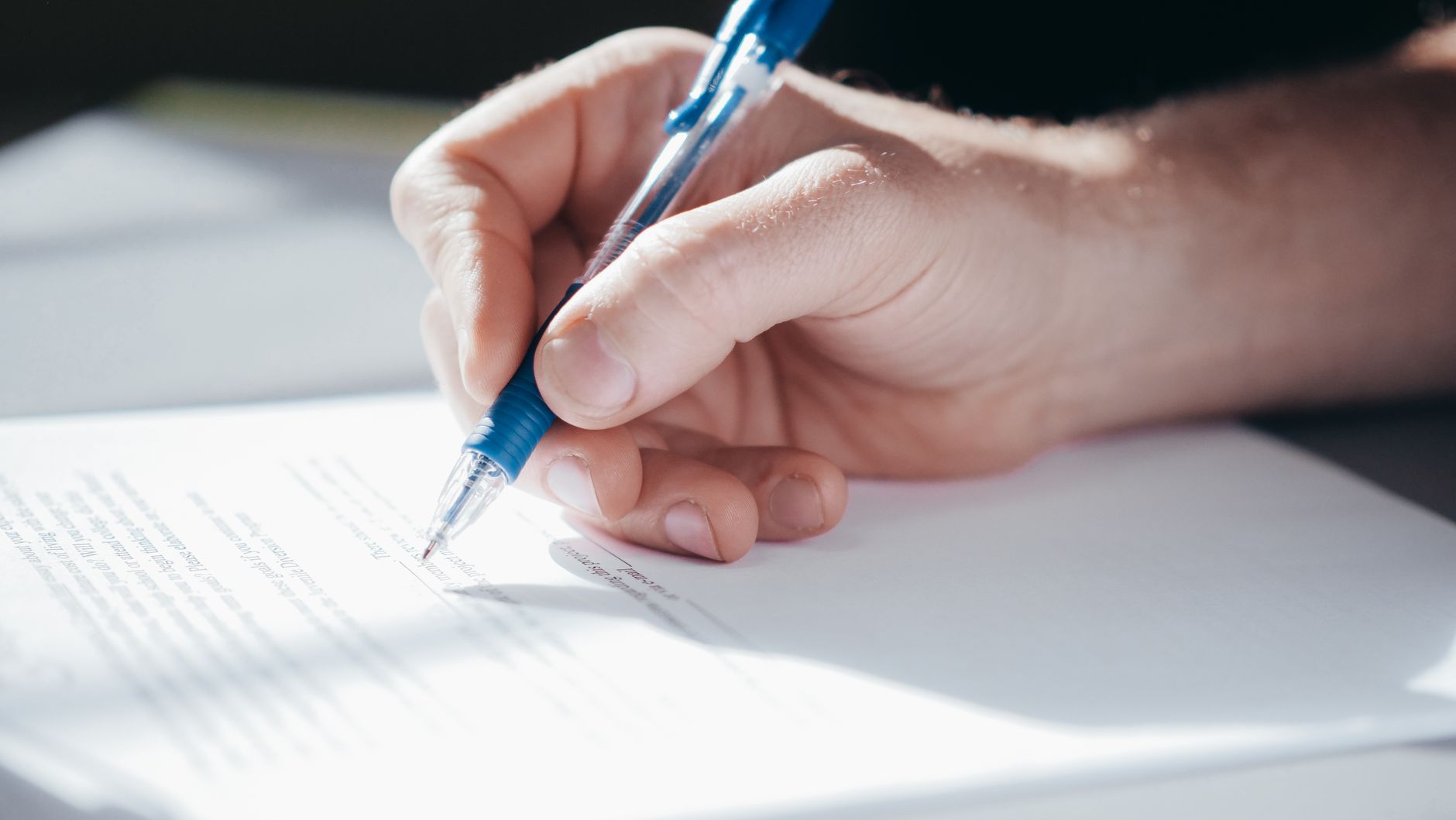 A detailed shot of a hand writing with a blue pen on a piece of paper.