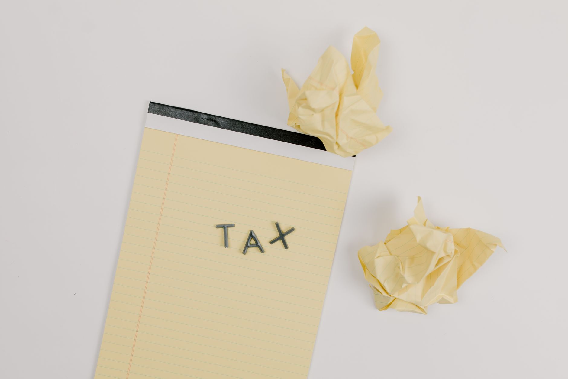 Flat lay of a notepad labeled 'tax' with crumpled paper on a white background, symbolizing financial stress.