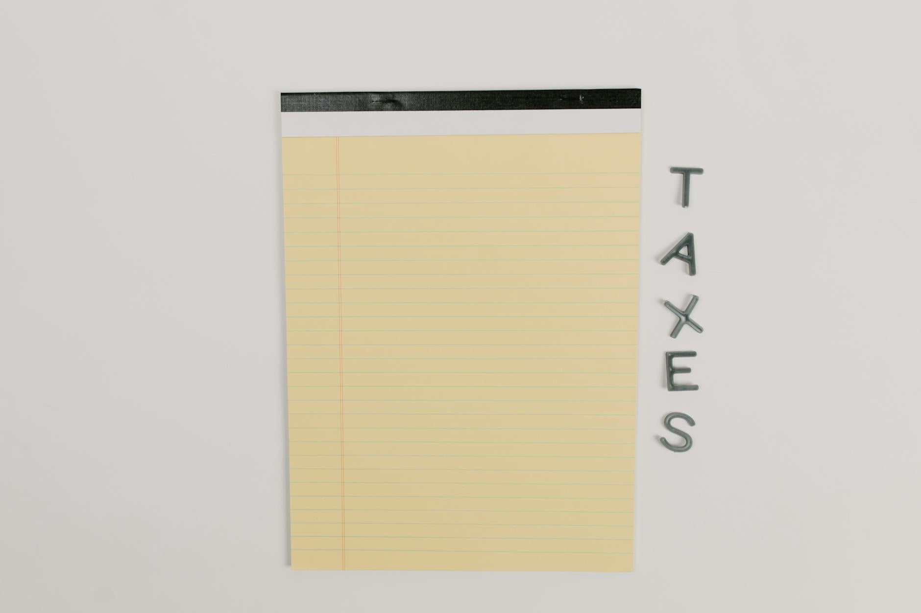 Close-up of a yellow legal pad and the word 'TAXES' on a white surface, ideal for finance themes.