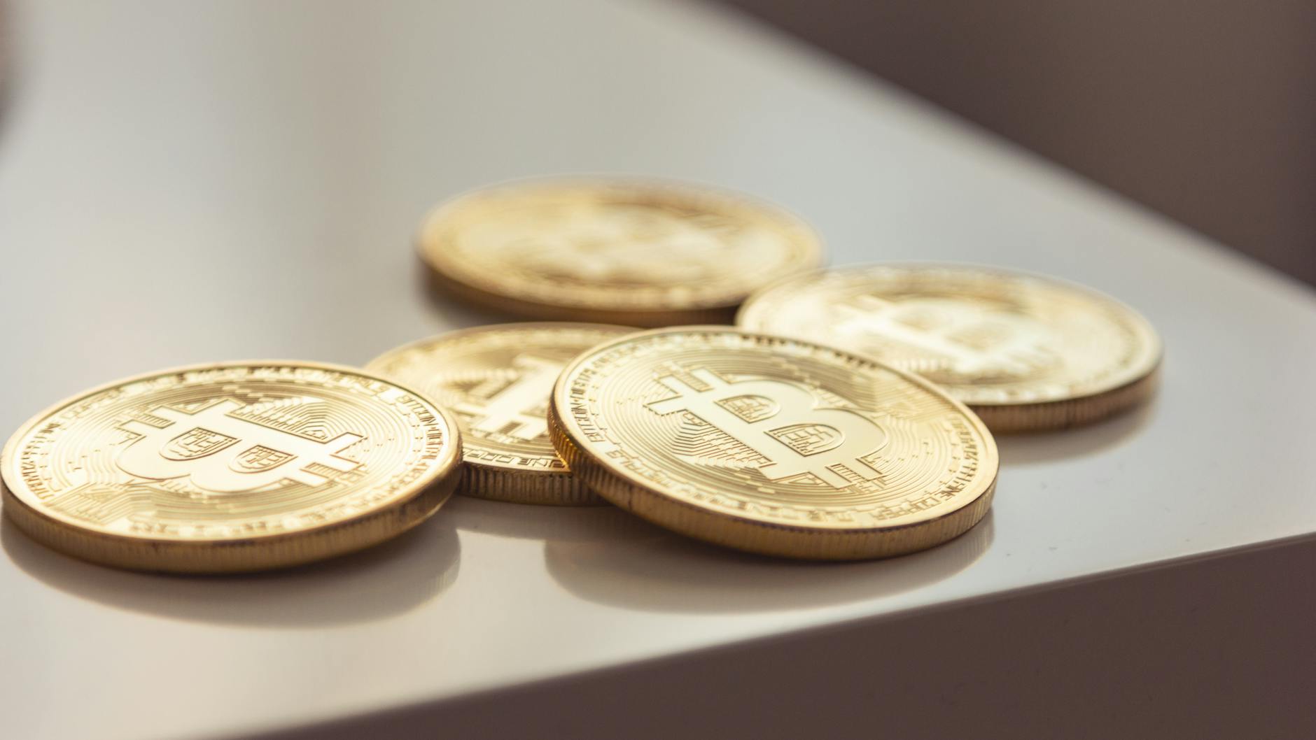 Close-up of shiny gold Bitcoin coins on white surface, symbolizing cryptocurrency wealth.
