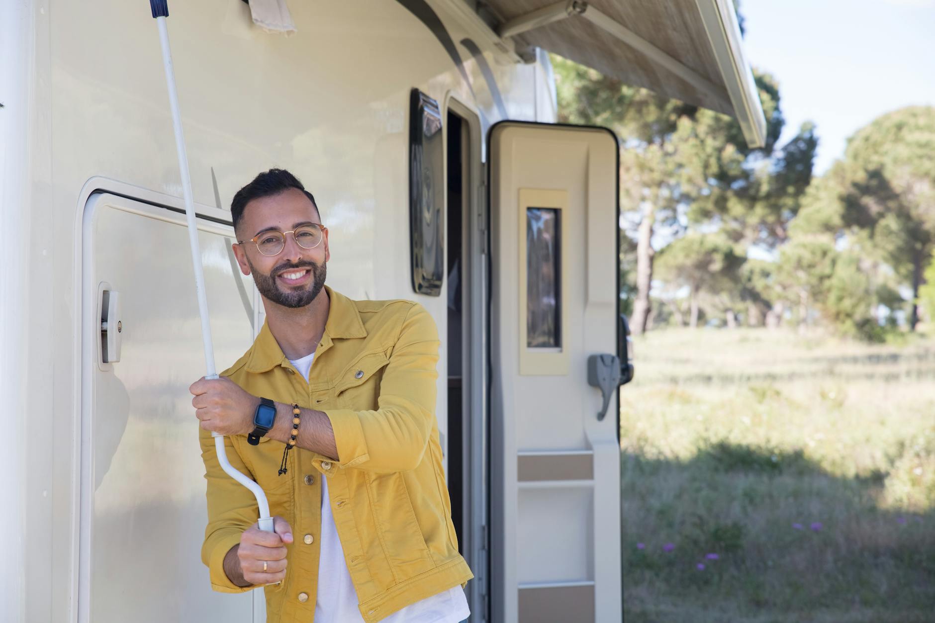 A smiling man in a yellow jacket relaxes by his camper van outdoors in Portugal.