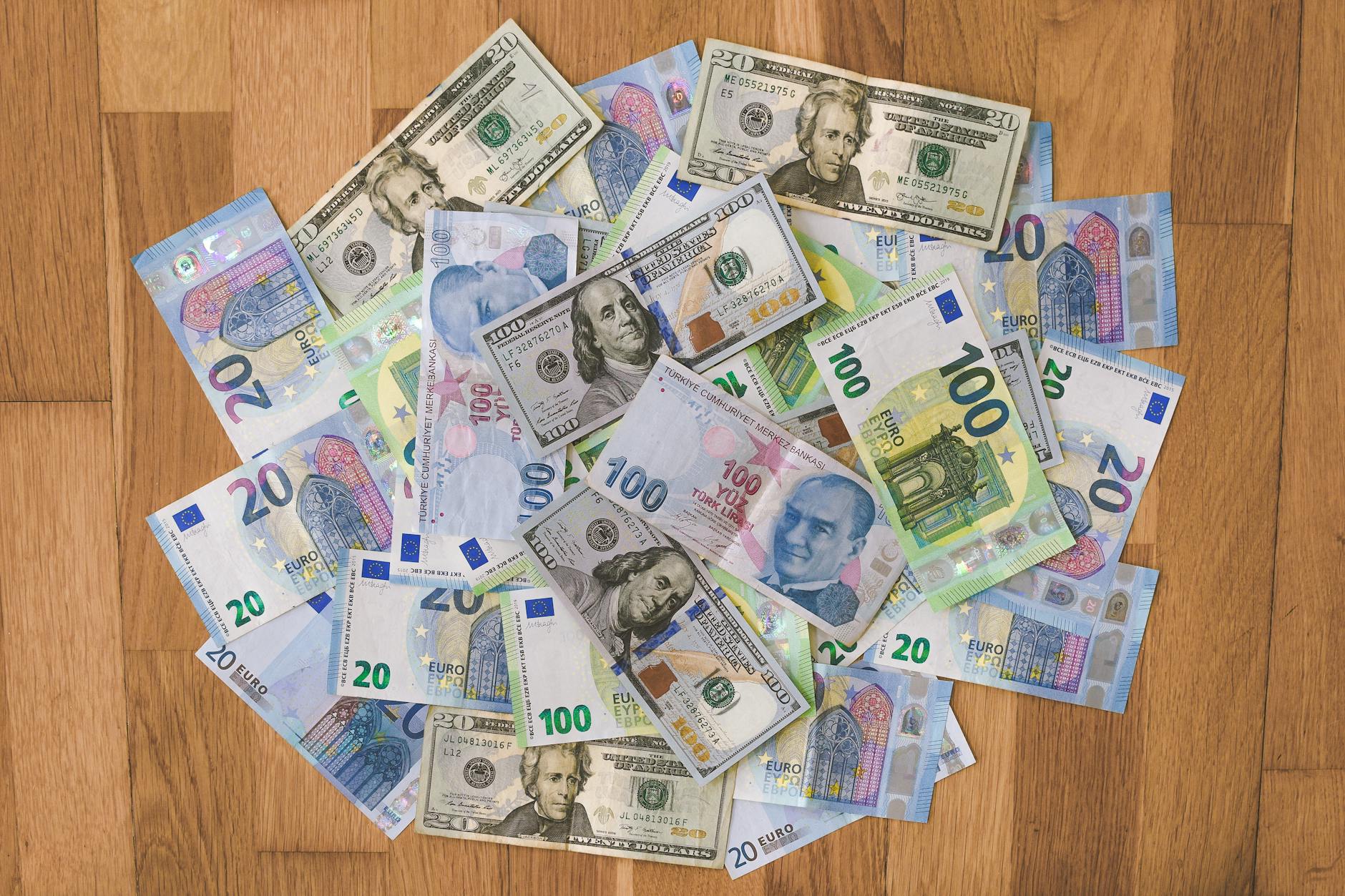 A collection of US dollars, euros, and Turkish lira banknotes on a wooden surface.